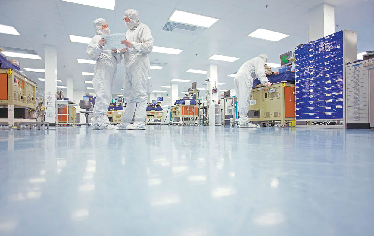 A low angle view of scientists in clean suits discussing a report in the silicon wafer manufacturing laboratory